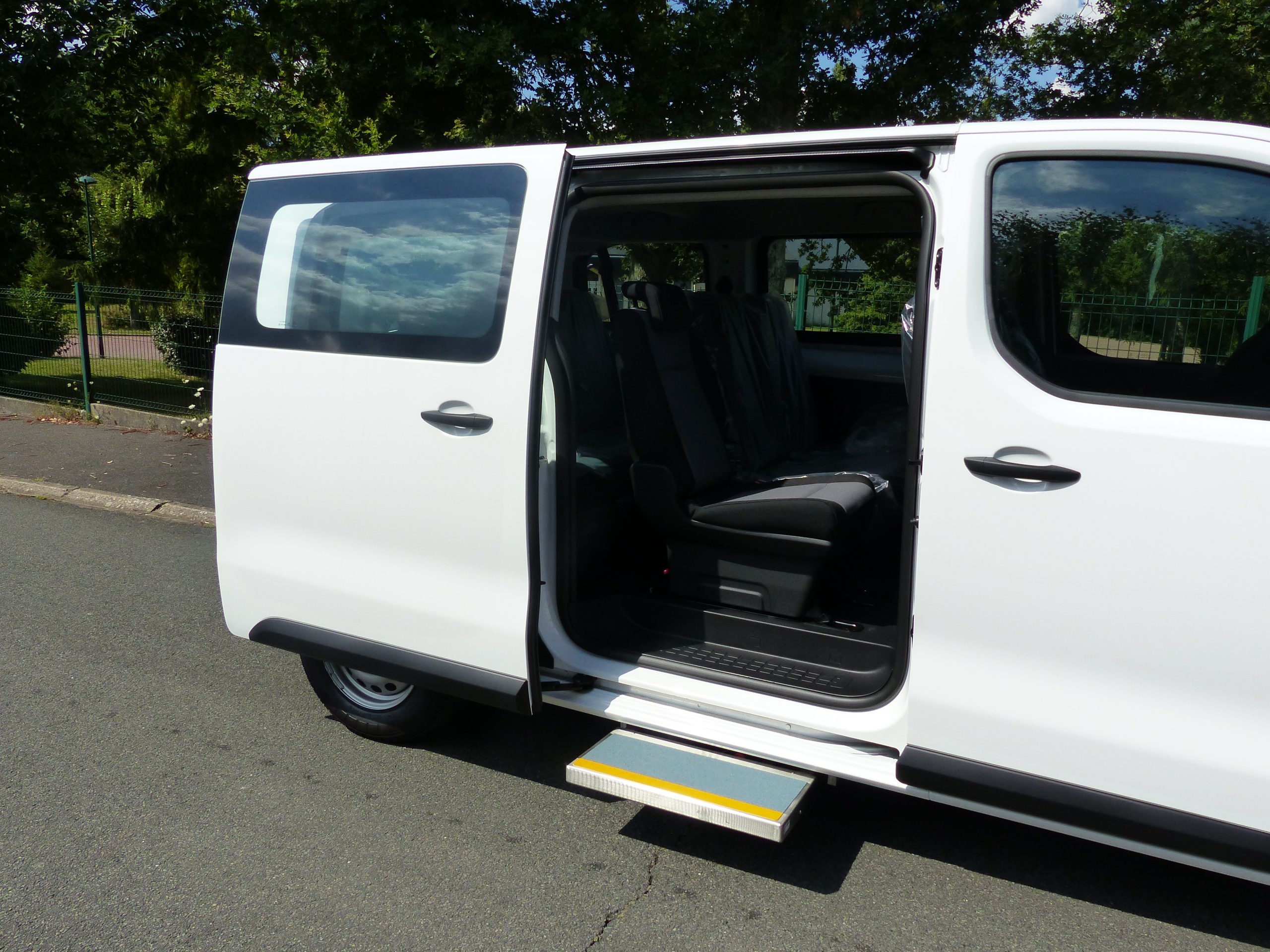 White passenger van with sliding side door open, showing interior seats and retractable step extended for easy access